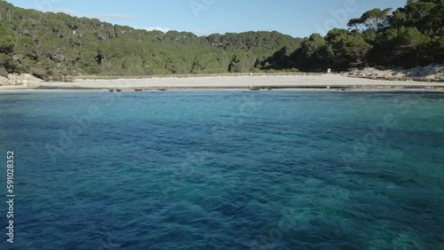 Drone flys low over water to Trebaluger beach in Spain with small secluded beach. photo