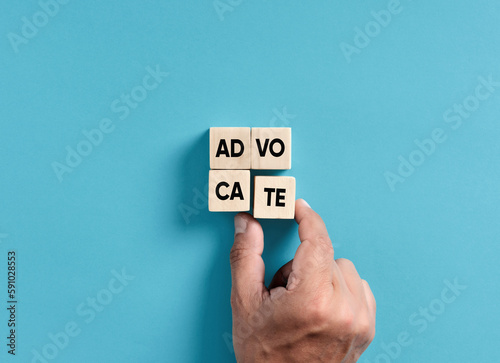 Male hand placing wooden blocks into a square shape to assemble the word advocate.