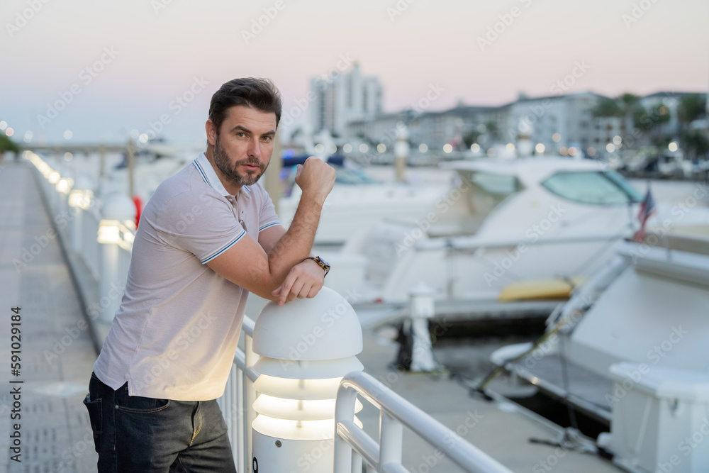 Rich businessman dreaming and thinking near the yacht. Urban fashion man in city walking street. Portrait of stylish handsome man outdoors. Portrait of attractive man walking on the street.