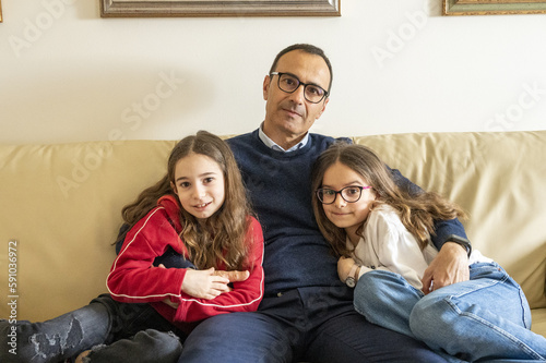 Padre con le figlie gemelle di nove anni sedute sul salotto di casa.