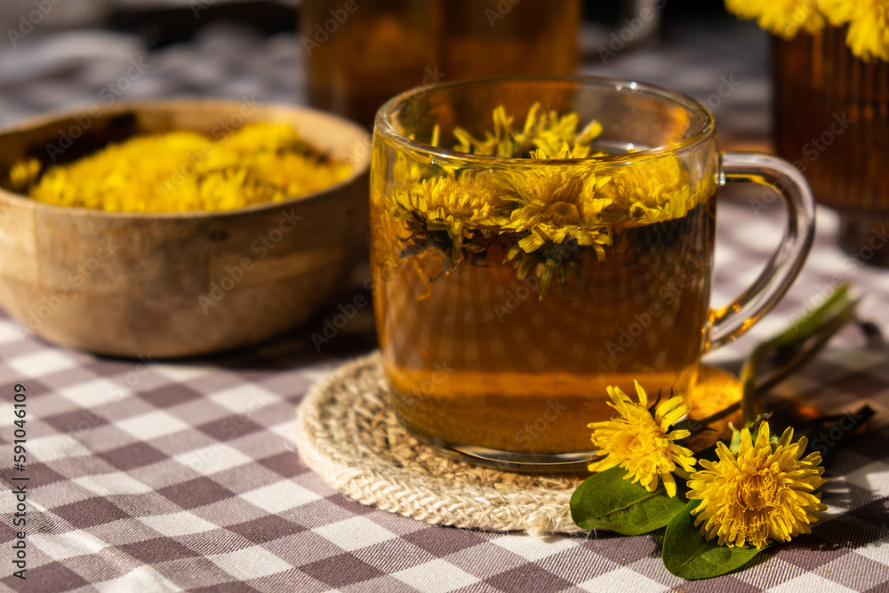 Dandelion flower healthy tea in glass cup on table. Herbal medicine Delicious tisane tea from with fresh yellow blossom dandelion flowers inside tea cup. Green clearing infusion Wildflowers Eco Dandelion flower healthy tea in glass cup on table. Herbal medicine Delicious tisane tea from with fresh yellow blossom dandelion flowers inside tea cup. Green clearing infusion Wildflowers Eco