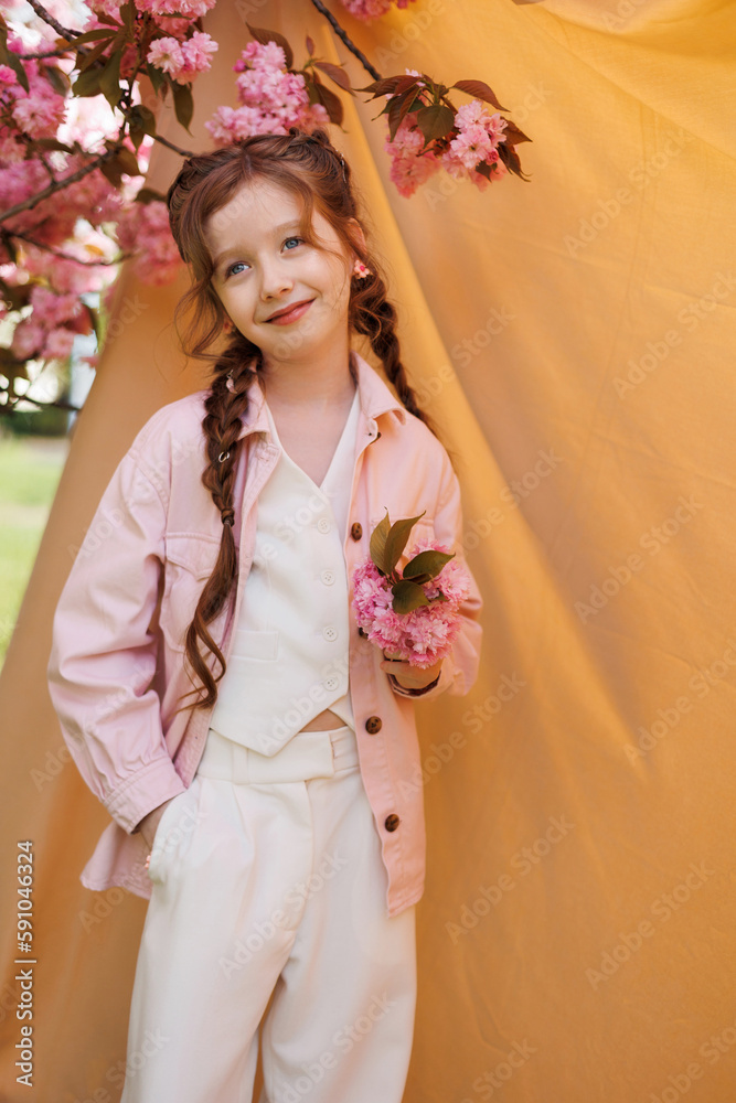 Playful girl in a good mood on a beige background and a branch of blooming sakura. Playful girl in a good mood on a beige background and a branch of blooming sakura.