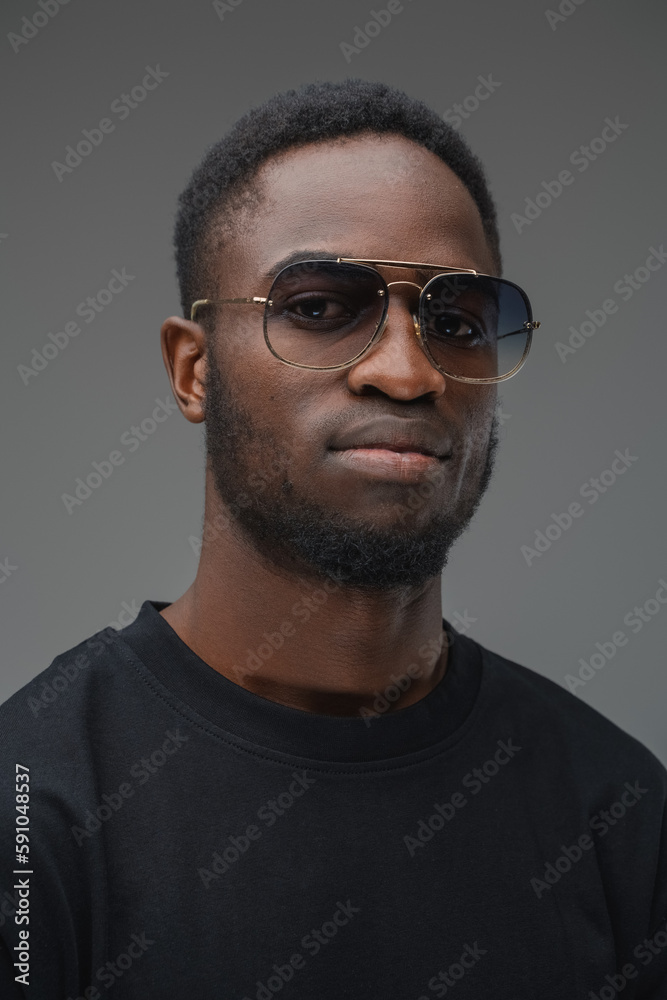 Shot of trendy black guy dressed in t shirt and sunglasses looking at camera.