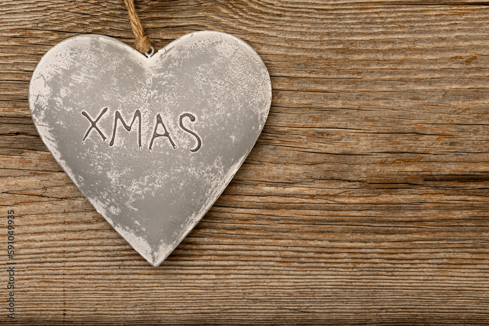 Fototapeta premium grey metal heart on rustic brown wooden background with free space for text and the letters XMAS