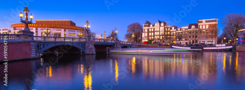 Blue bridge, Amsterdam, Netherlands. Blauwbrug. Evening cityscape. Blue sky and city lights. Dutch canals. Reflections on the surface of the water. Photography for design and wallpaper.