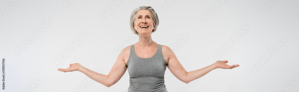 satisfied senior woman with grey hair looking up and gesturing isolated on grey, banner. satisfied senior woman with grey hair looking up and gesturing isolated on grey, banner.