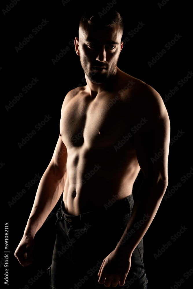 Silhouette of a muscular shirtless man in the shadow on a black studio background