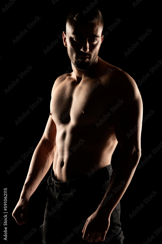 Silhouette of a muscular shirtless man in the shadow on a black studio background Silhouette of a muscular shirtless man in the shadow on a black studio background