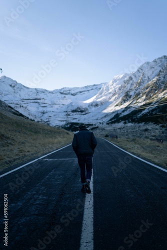 Vertical shot of a man walking along an asphalt road against the snowy hills