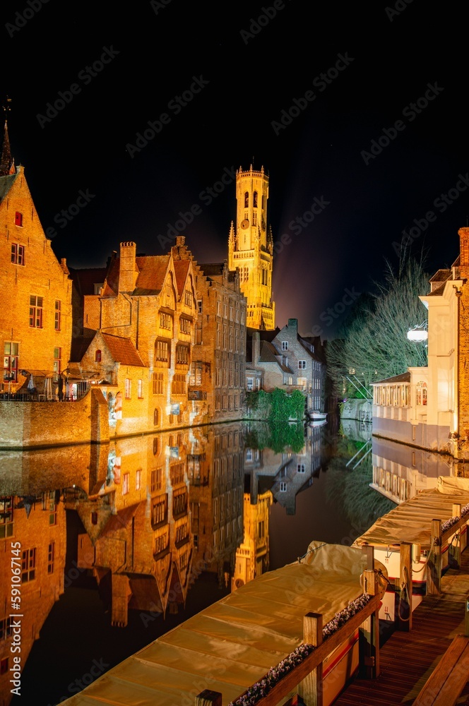 Vertical view of the old traditional buildings reflecting in water at night in Bruges, Belgium