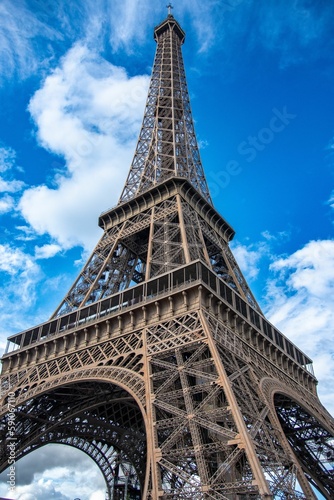 Vertical low angle shot of the Eiffel Tower against a blue cloudy sky in Paris, France