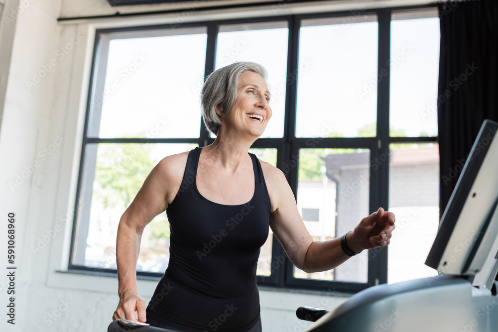 overjoyed senior woman with grey hair running on treadmill in gym. overjoyed senior woman with grey hair running on treadmill in gym.