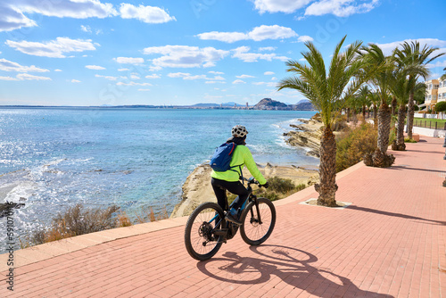 nice senior woman cycling on a cool spring day with her electric bicycle at the waterfront of Alicante  Costa Blanca  Spain