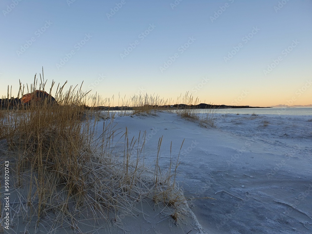Lakeshore covered in snow at sunset with orange and blue sky in the background Lakeshore covered in snow at sunset with orange and blue sky in the background