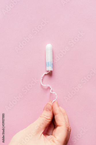 Feminine sanitary tampon on pink background. Woman s hand with a tampon. Hygiene care during critical days  caring for women s health. Monthly protection. copyspace. menstrual cycle.