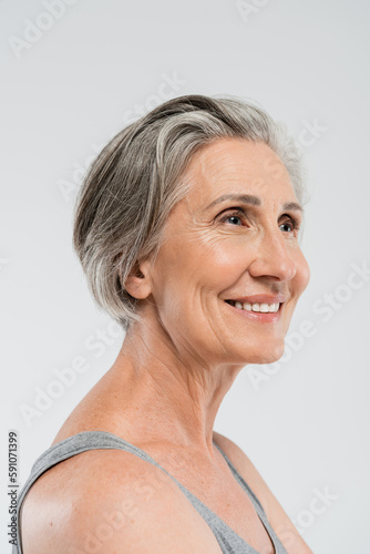 portrait of happy senior woman with grey hair standing and looking away isolated on grey.