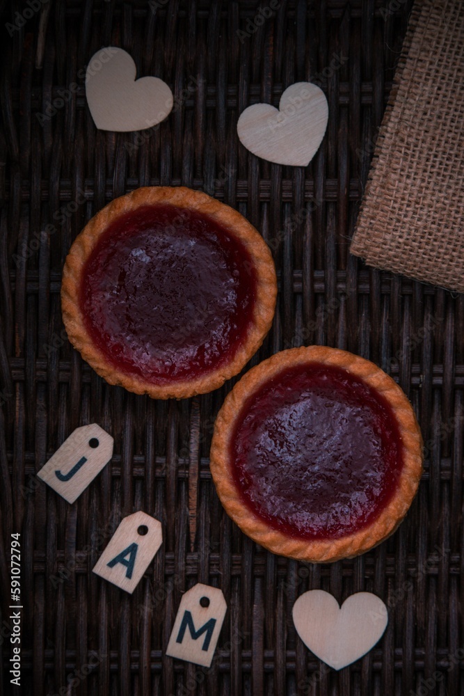 High-angle shot of two small cakes with red jam on them with white letters and hearts.