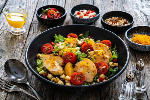 Tasty Greek salad - fried chicken breast, halloumi cheese, oranges, pine nuts, raisins, mini tomatoes and fresh green vegetables on wooden background 