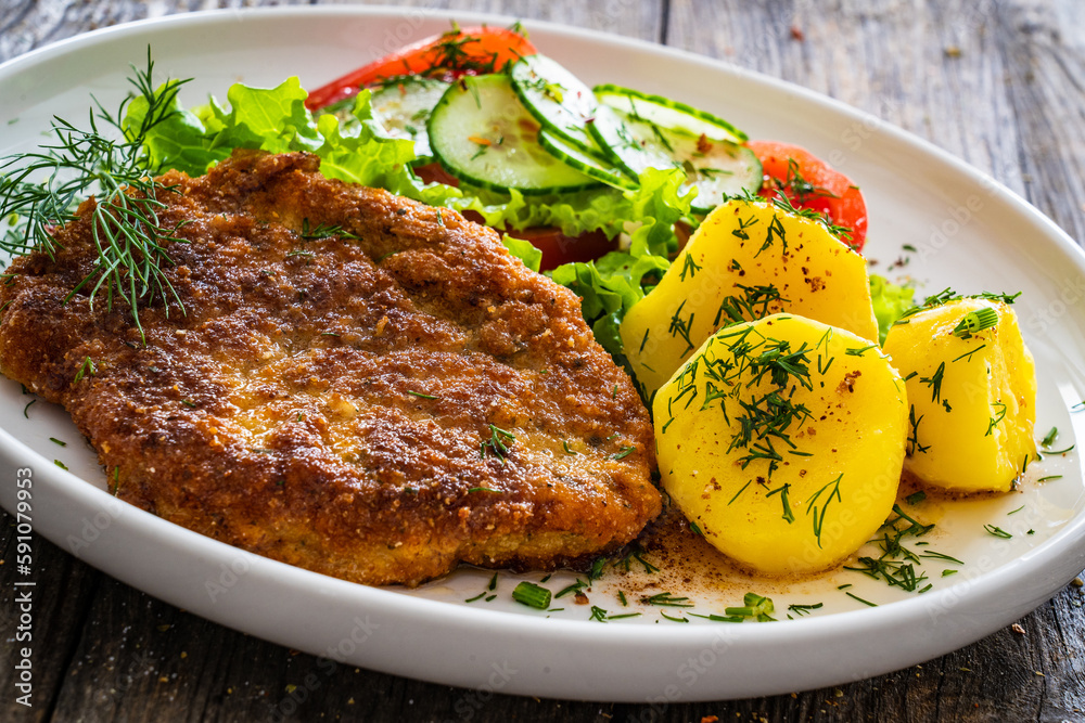 Breaded fried pork chop with fresh vegetable salad and potatoes on wooden table
Breaded fried pork chop with fresh vegetable salad and potatoes on wooden table