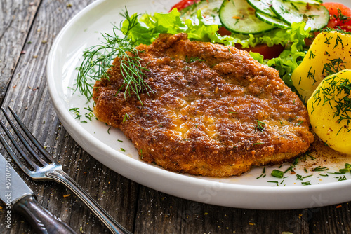 Breaded fried pork chop with fresh vegetable salad and potatoes on wooden table 