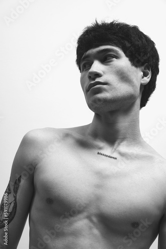 Black and white photography. Portrait of young handsome asian man with tattoo, posing shirtless. Deep serious look away. Concept of male body aesthetics, style, fashion, health, men's beauty