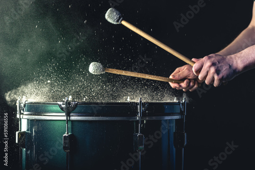 A man plays a musical percussion instrument with sticks on a dark background. photo