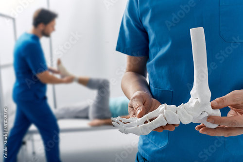 Valokuvatapetti Podiatrist showing anatomical foot skeleton model during his assistant examinati