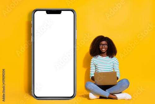 Full body portrait of attractive charming lady sit floor use wireless netbook huge phone display isolated on yellow color background