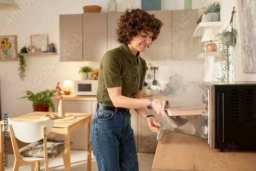 Fotografie Young housewife taking burnt food out of the oven during cooking in the kitchen