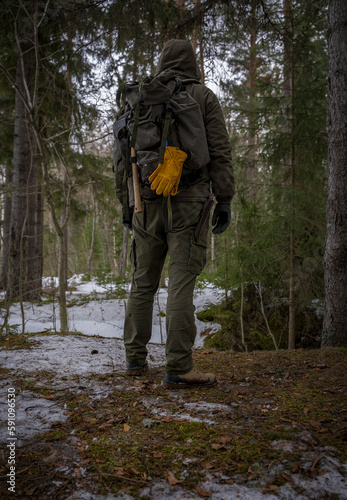 Brutal man traveler stands back in the woods with a backpack behind his back. The concept of surviving in the wild.