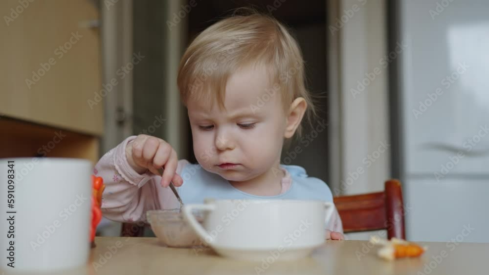 The child is eating in the kitchen. A small child learned to eat with a spoon by himself. The child is one year and eight months old. The child is eating in the kitchen. A small child learned to eat with a spoon by himself. The child is one year and eight months old.