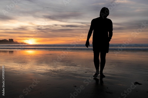 a person walking along the beach with their surfboard at sunset