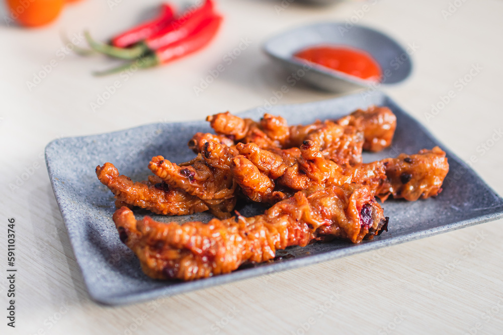 Spicy chicken feet or ceker ayam pedas with chili, tomato and sauce served with a plate on wooden white table