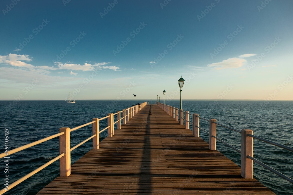 Long wooden pier surrounded by the clam waters of the blue ocean with the horizon in the background Long wooden pier surrounded by the clam waters of the blue ocean with the horizon in the background