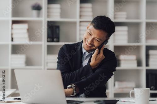 Happy working asian businessman talking on the phone with accounting documents at desk in happy working office