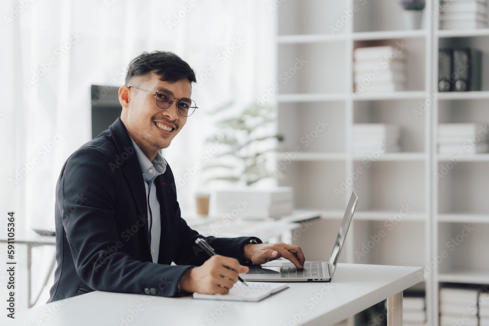 Happy working asian businessman talking on the phone with accounting documents at desk in happy working office