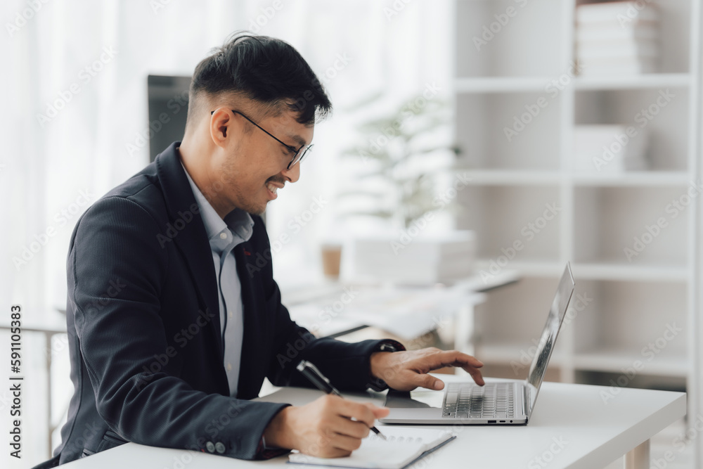 Happy working asian businessman talking on the phone with accounting documents at desk in happy working office Happy working asian businessman talking on the phone with accounting documents at desk in happy working office