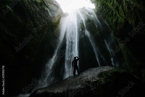 Low angle shot of a person against a waterfall in green mountains on a cloudy day in Iceland