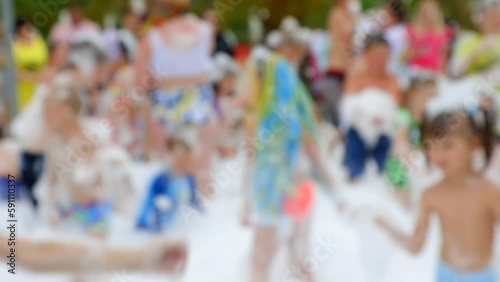 Crowd of children and adults have fun in white foam at a foamy party in the hot summer at an amusement park. Children catch foam and soap bubbles with their hands at a summer holiday
