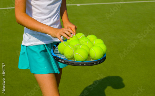 young girl tennis player collect tennis balls after training on the grass court on a sunny day