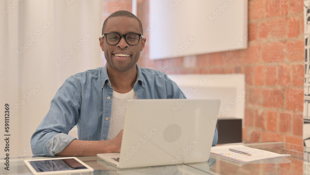 African Man Smiling at Camera while Working on Laptop