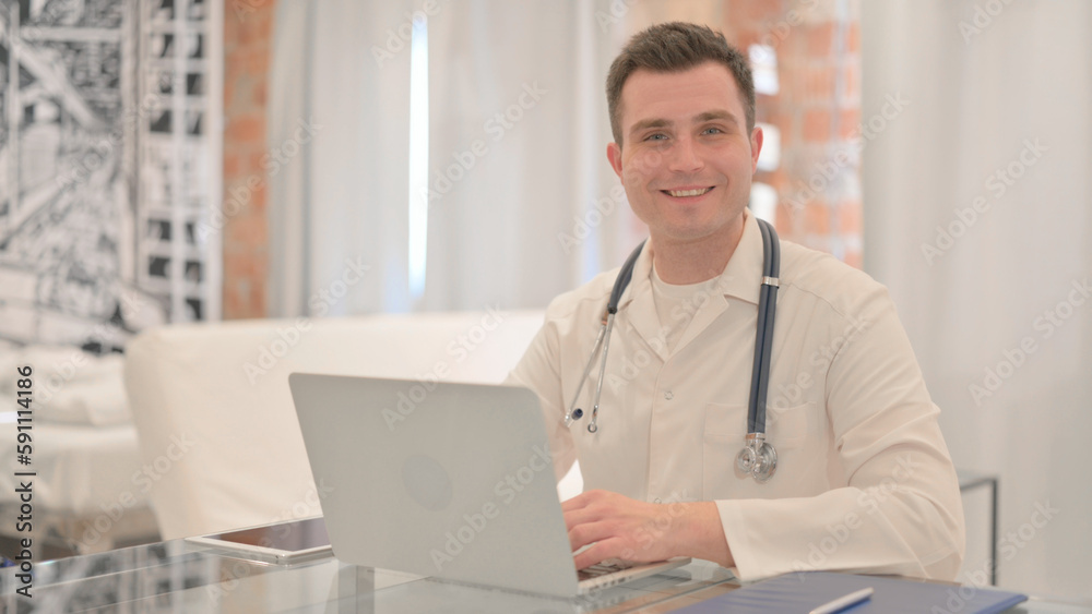Male Doctor Smiling at Camera while Working on Laptop Male Doctor Smiling at Camera while Working on Laptop