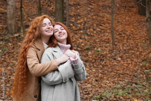 Portrait of beautiful young redhead sisters in park on autumn day. Space for text