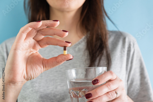 Fotografi Woman taking gastritis, stomach ulcer, heartburn medicine capsule or pill on blu