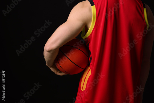 Athletic man with basketball ball on black background, closeup