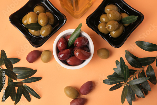 Bottle of oil, olives and tree twigs on orange background, flat lay