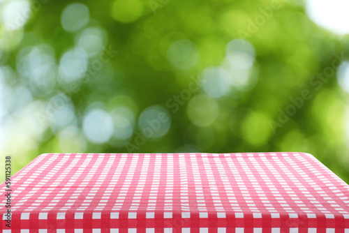 Red and white checkered tablecloth on table against green blurred background. Space for design