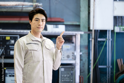Image of a man in a factory posing for the point in his work clothes, looking at the camera. right copyspace
