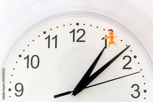 Biological clock: time pressure to have kids. Close up of clock with baby toy. Alarm for parenthood