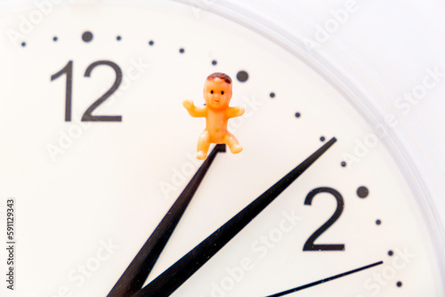 Biological clock: time pressure to have kids. Close up of clock with baby toy. Alarm for parenthood